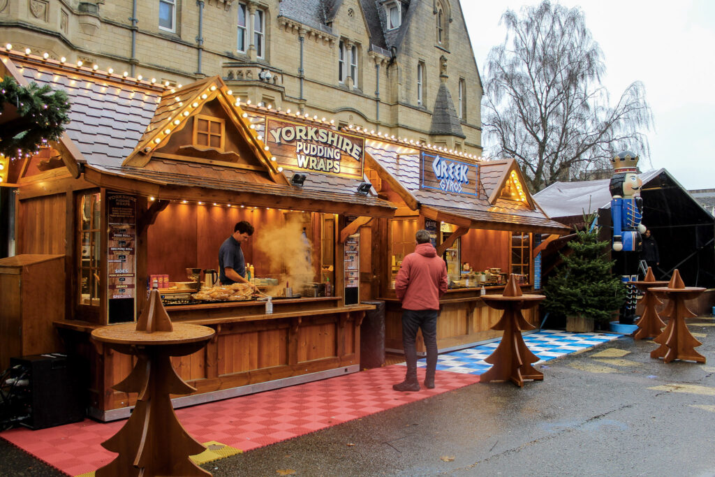 A wooden style street food chalet adorned with festive lighting selling Yorkshire Pudding Wraps.