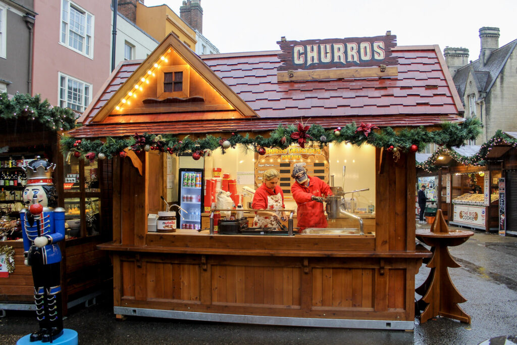 A wooden style street food chalet adorned with festive lighting selling Churros